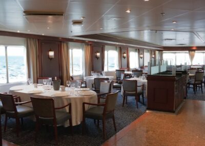 Restaurant der MS Discoverer mit gedeckten Rundtischen und Fenstern zum Meer