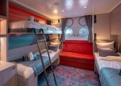 Triple cabin on the MS Hondius with a bunk bed, a single bed, a red sofa, and two portholes