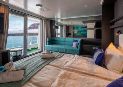 Grand Suite on the MS Hondius with a double bed, sofa, and glass door leading to a private balcony with a view of the sea