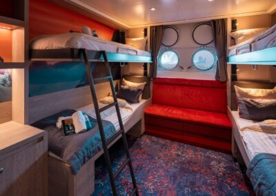 Four-bed cabin on the MS Hondius with two bunk beds, a red sofa, and two portholes