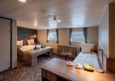 Superior-Kabine der MS Plancius mit Doppelbett, Schlafsofa, Tisch und zwei Fenstern