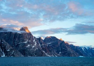 A rugged mountain range along the coast of Greenland in the evening light