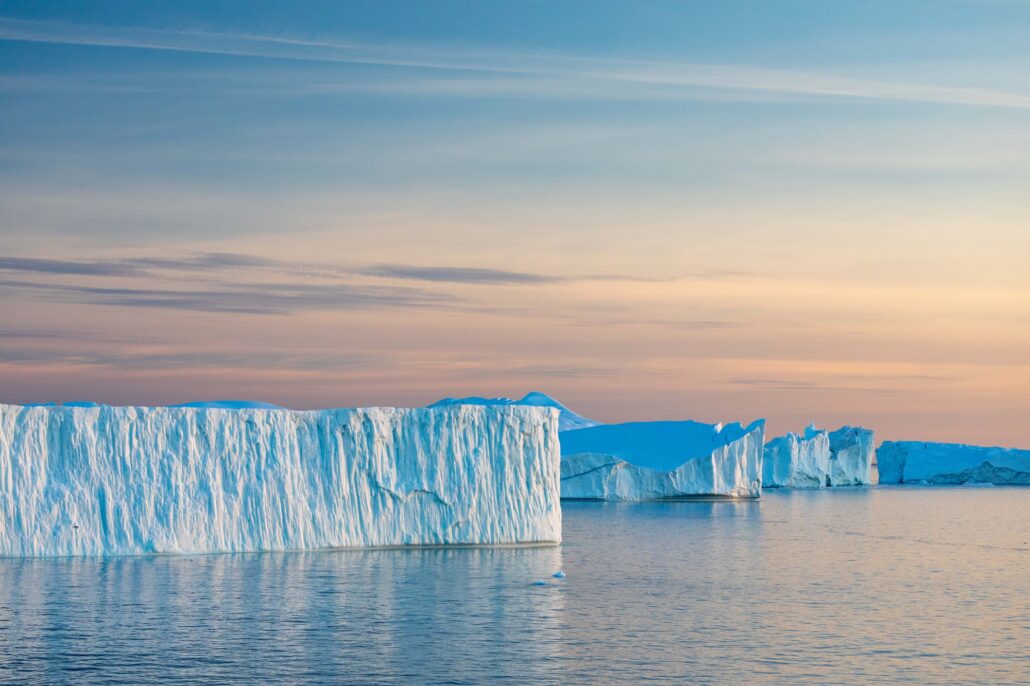 Eiswand des Ilulissat-Eisfjords im Abendlicht über spiegelndem Wasser