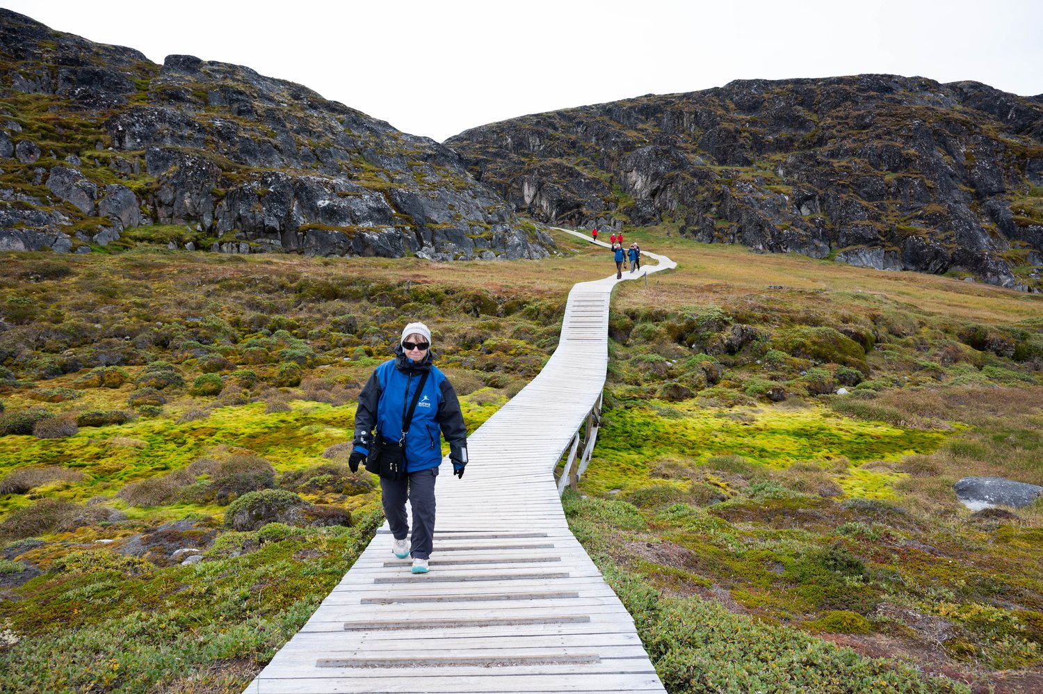 Wanderin auf dem Holzsteg über die Tundra zum Eisfjord von Ilulissat Hiker on the wooden boardwalk across the tundra toward the Ilulissat Icefjord