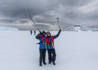 Two passengers on the snow in Wilhelmina Bay, with the expedition ship in the background