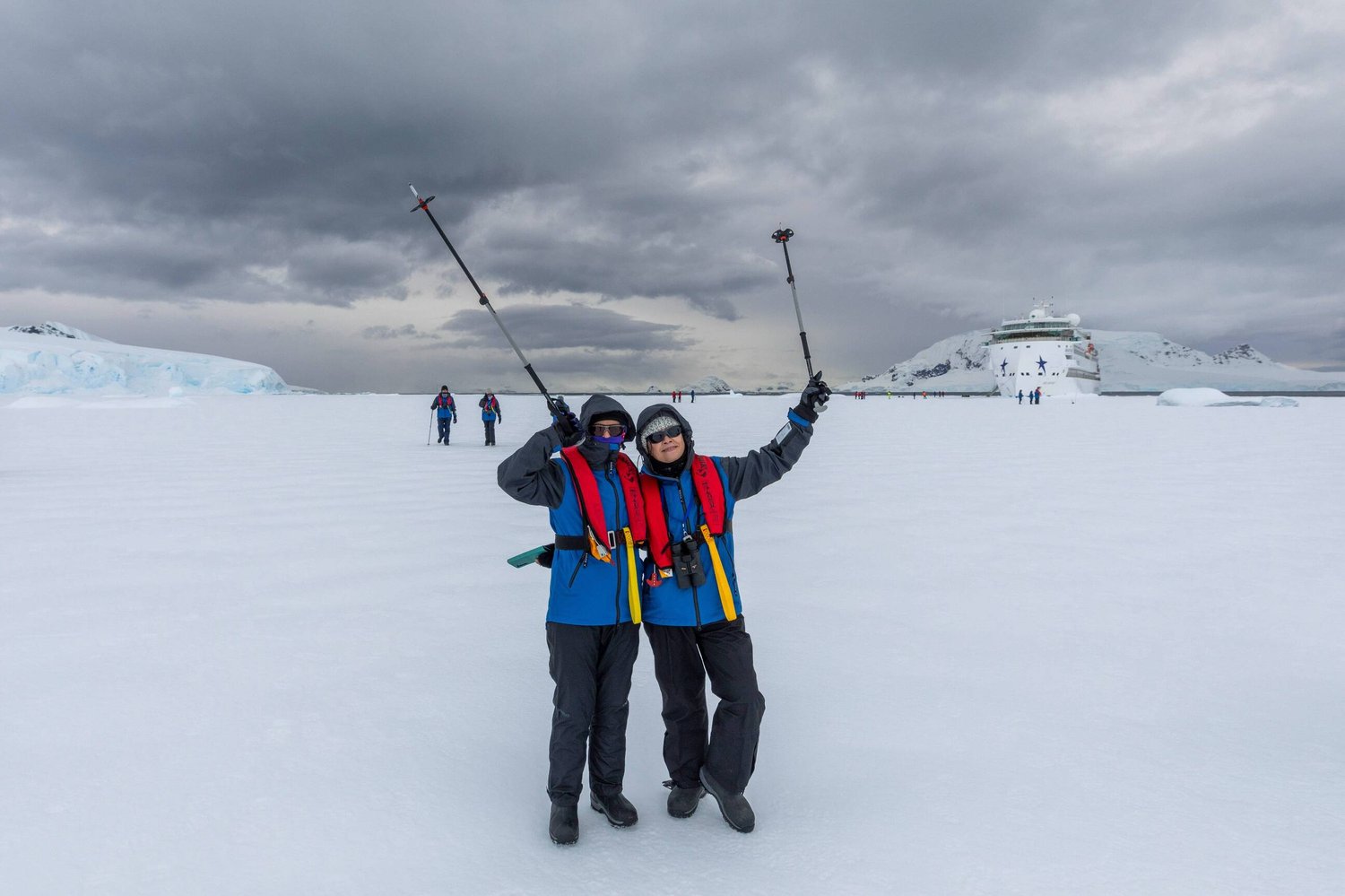 Zwei Passagiere auf dem Schnee der Wilhelmina Bay, im Hintergrund das Expeditionsschiff